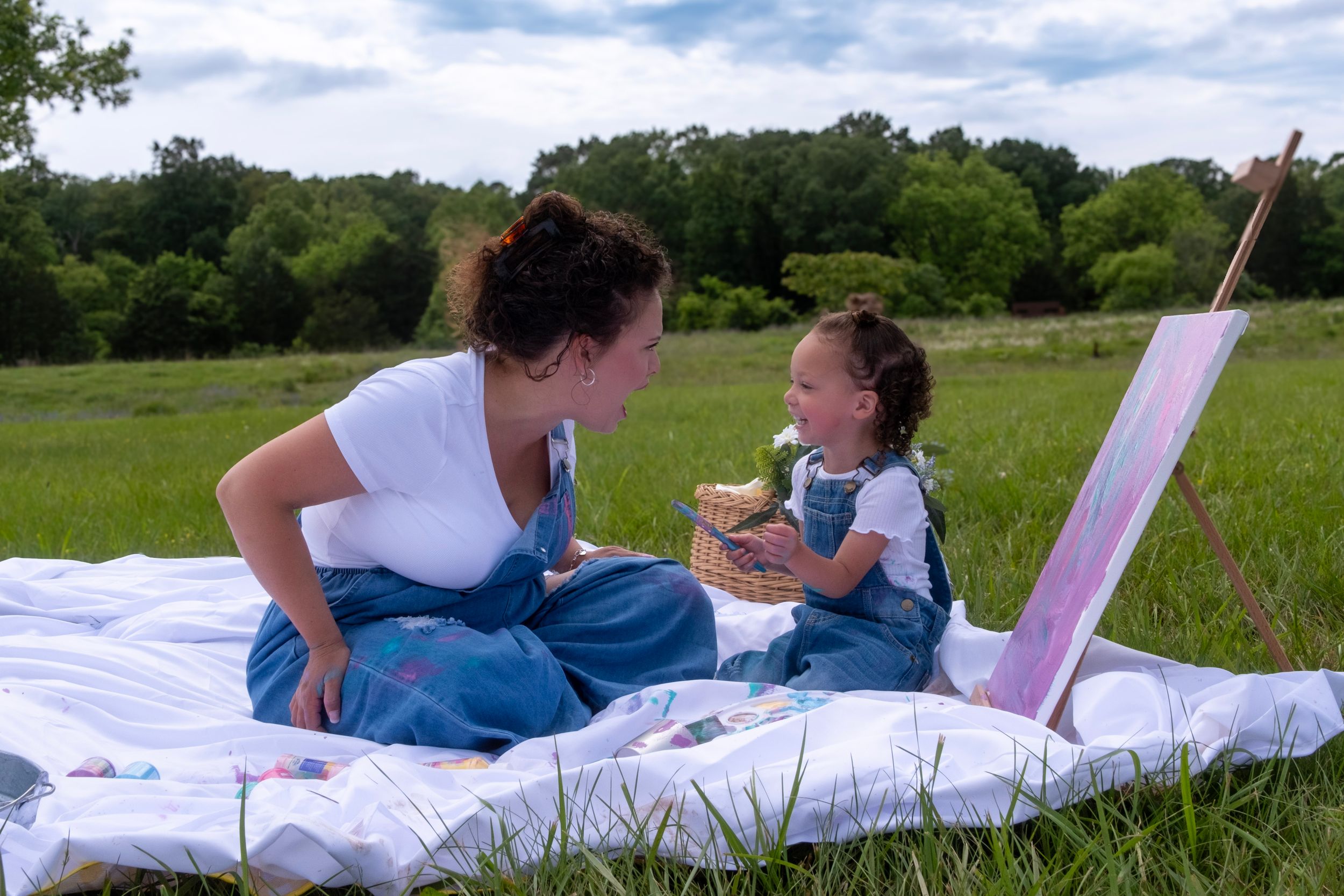 A group enjoys a summer picnic on a white blanket in a sunny green field with blue skies.