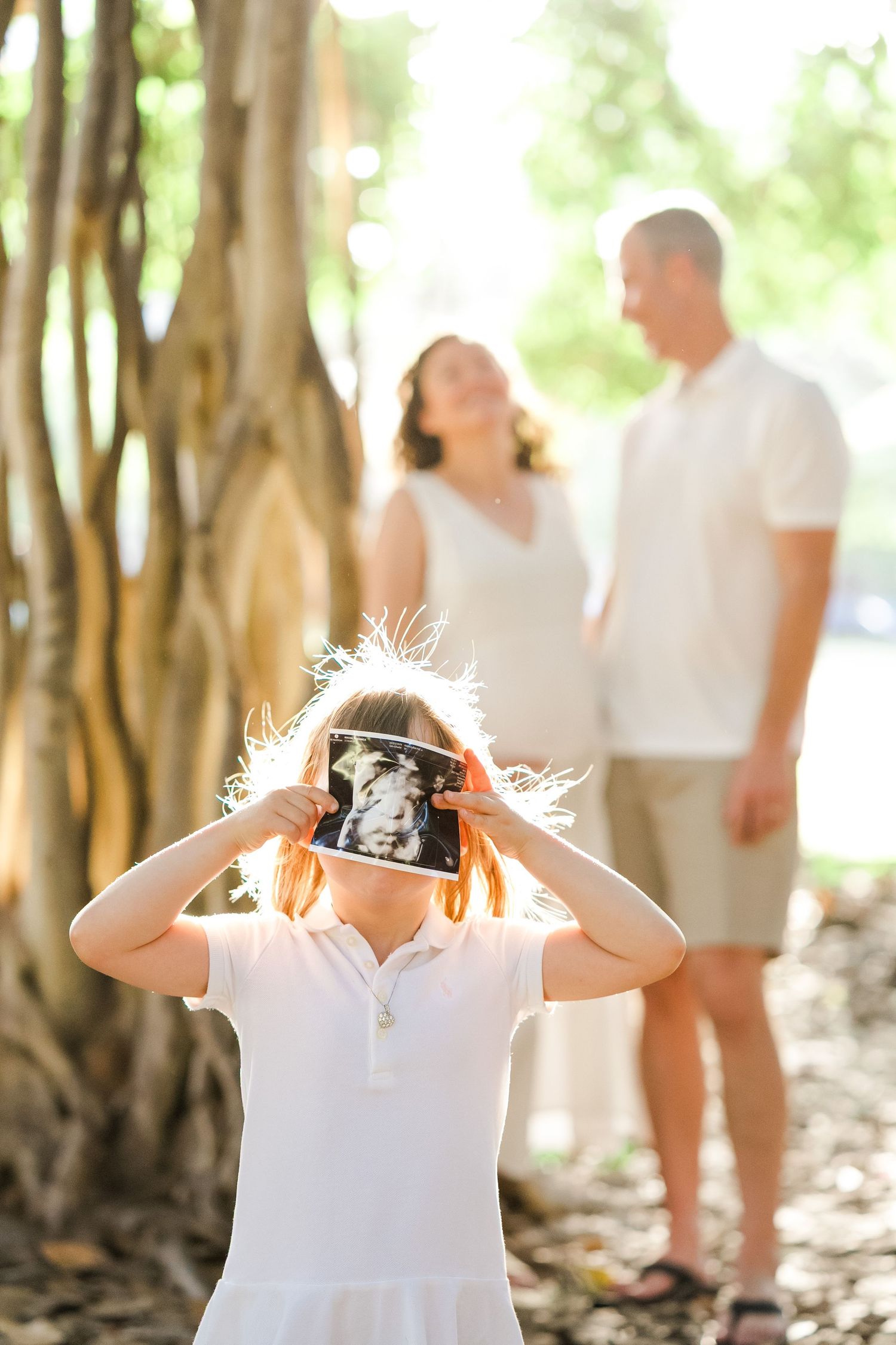 Serene silhouette of an expectant mother in a flowing white dress standing on a beach at sunset. Oahu family photographer