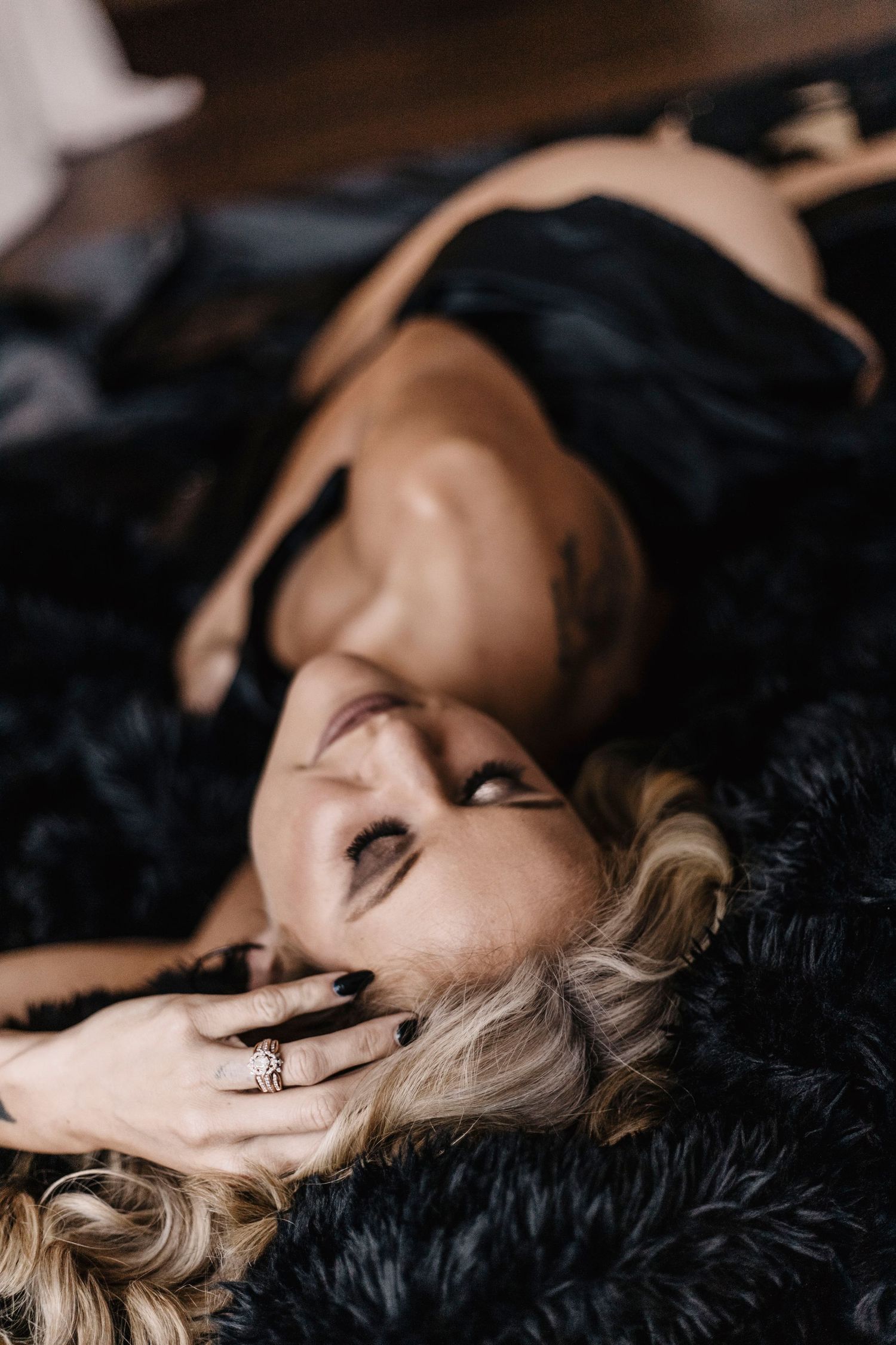 Artistic portrait of someone lying on black fur with blonde hair and expressive hand gesture near face.