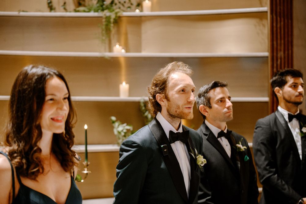 A row of formally dressed people stand together at a wedding ceremony with boutonnieres and elegant attire.