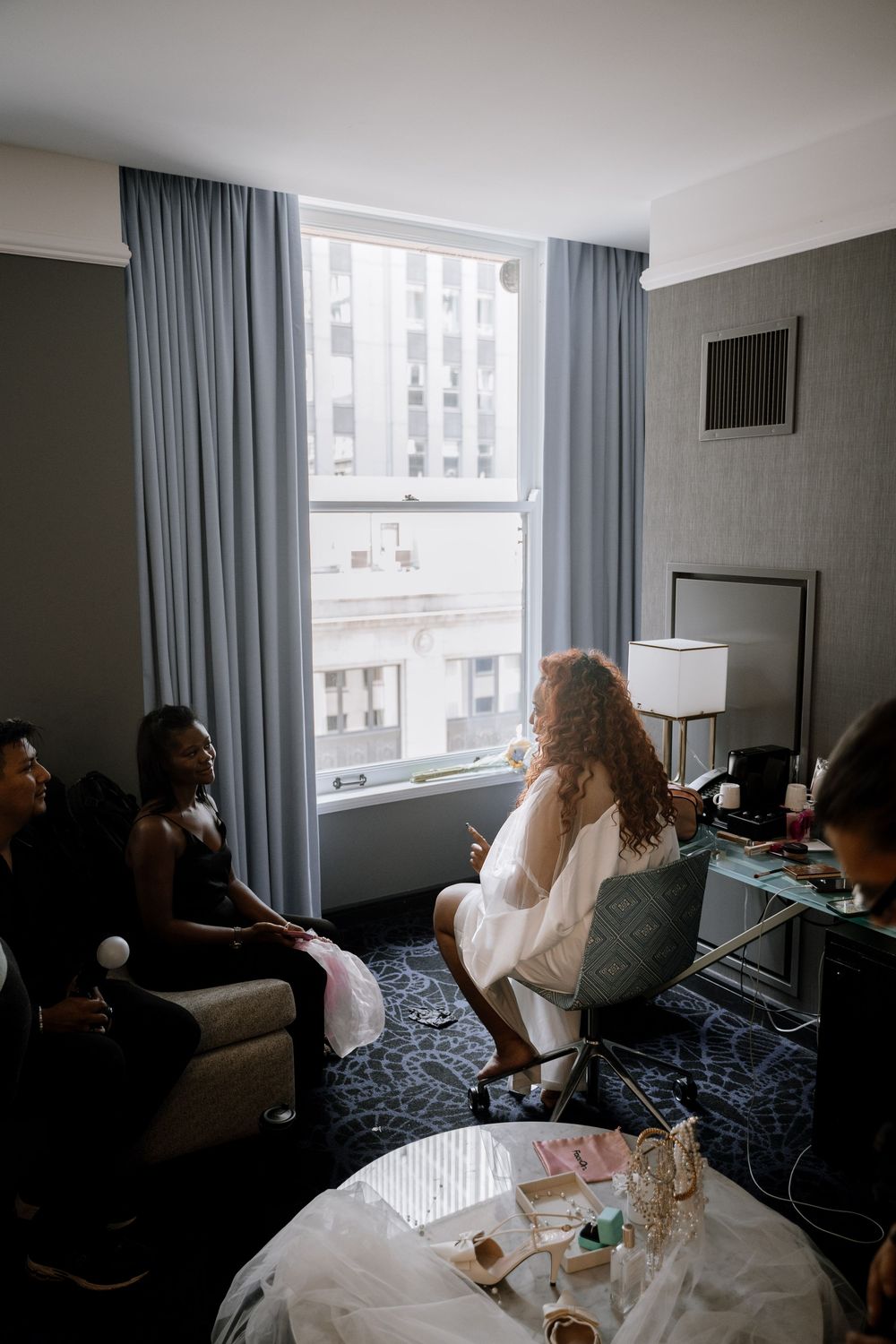 A group of people sitting in a hotel room with large windows, blue curtains and modern furnishings.