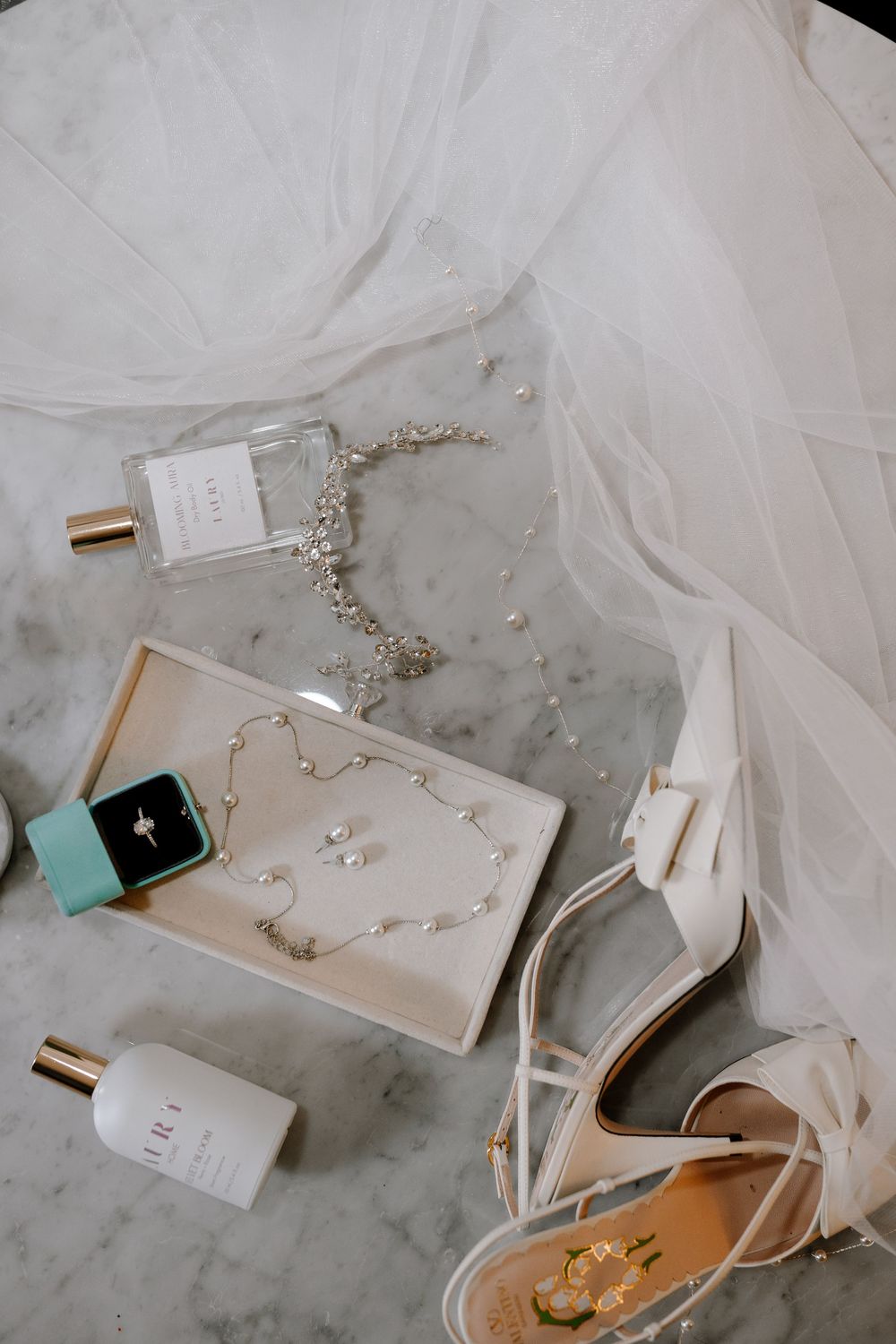 Elegant wedding accessories including jewelry, perfume, and delicate white tulle arranged on luxurious marble.