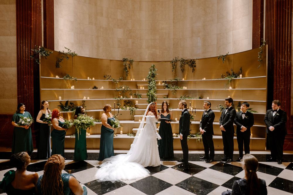 A wedding ceremony takes place in an elegant venue with black and white checkered floors and golden walls.