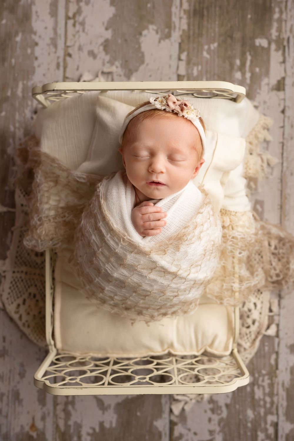 Baby girl in cream bed on wood floor, taken by Jen Knightstep, Photographer