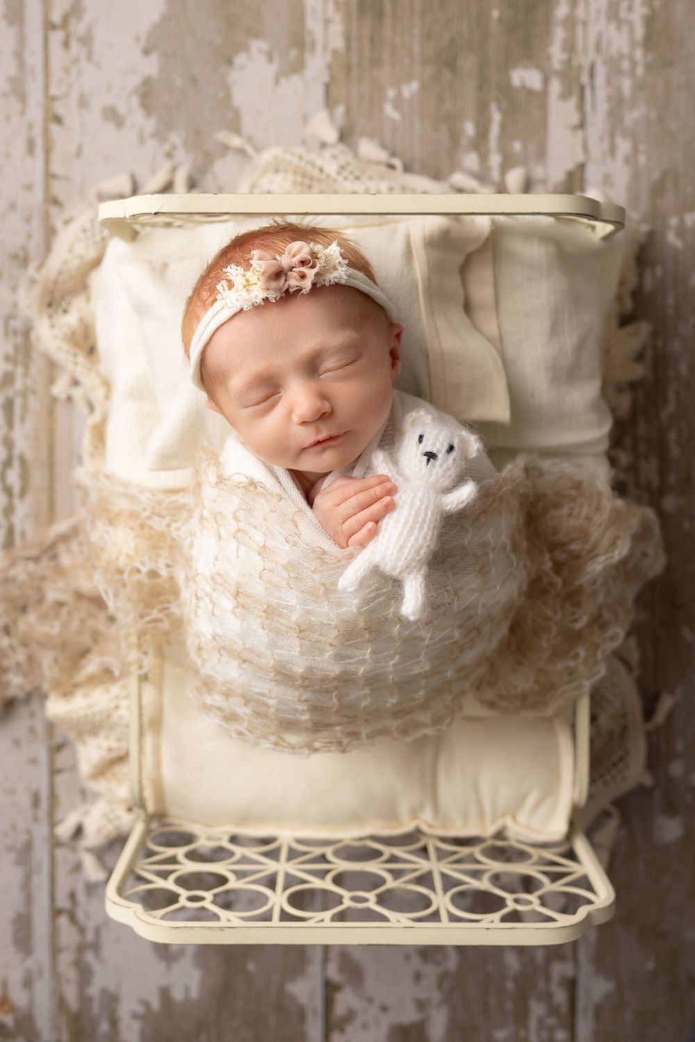 Baby girl in cream bed on wood floor, taken by Jen Knightstep, Photographer