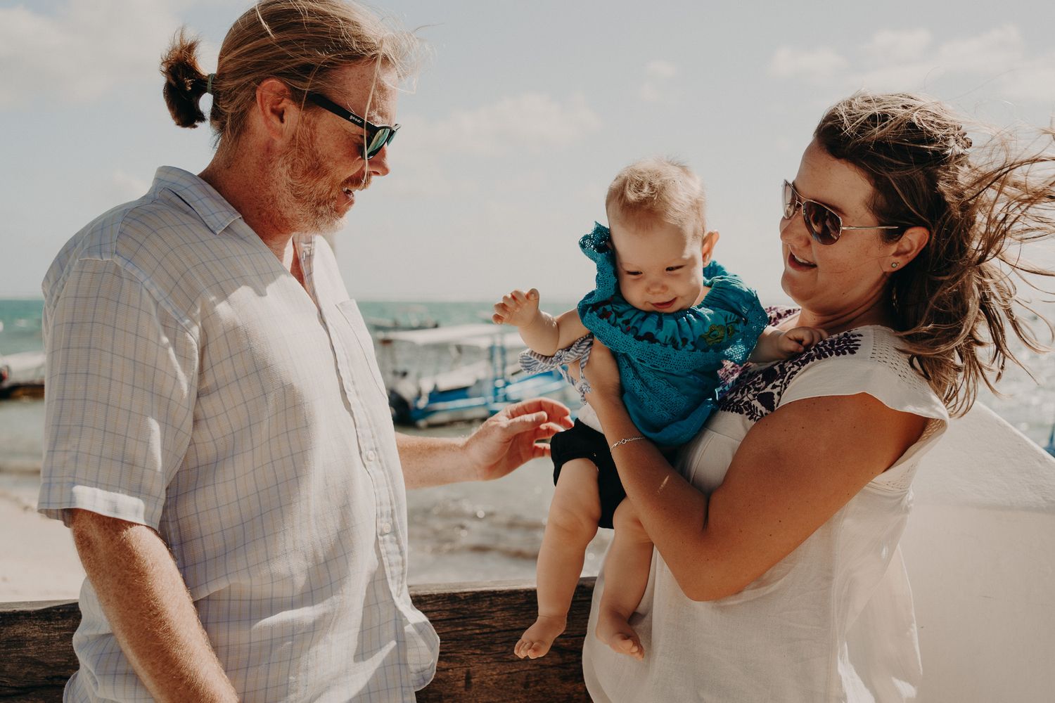 A family walks together along a sunny beach with sand and ocean waves in the background. Puerto Morelos Family Photography.