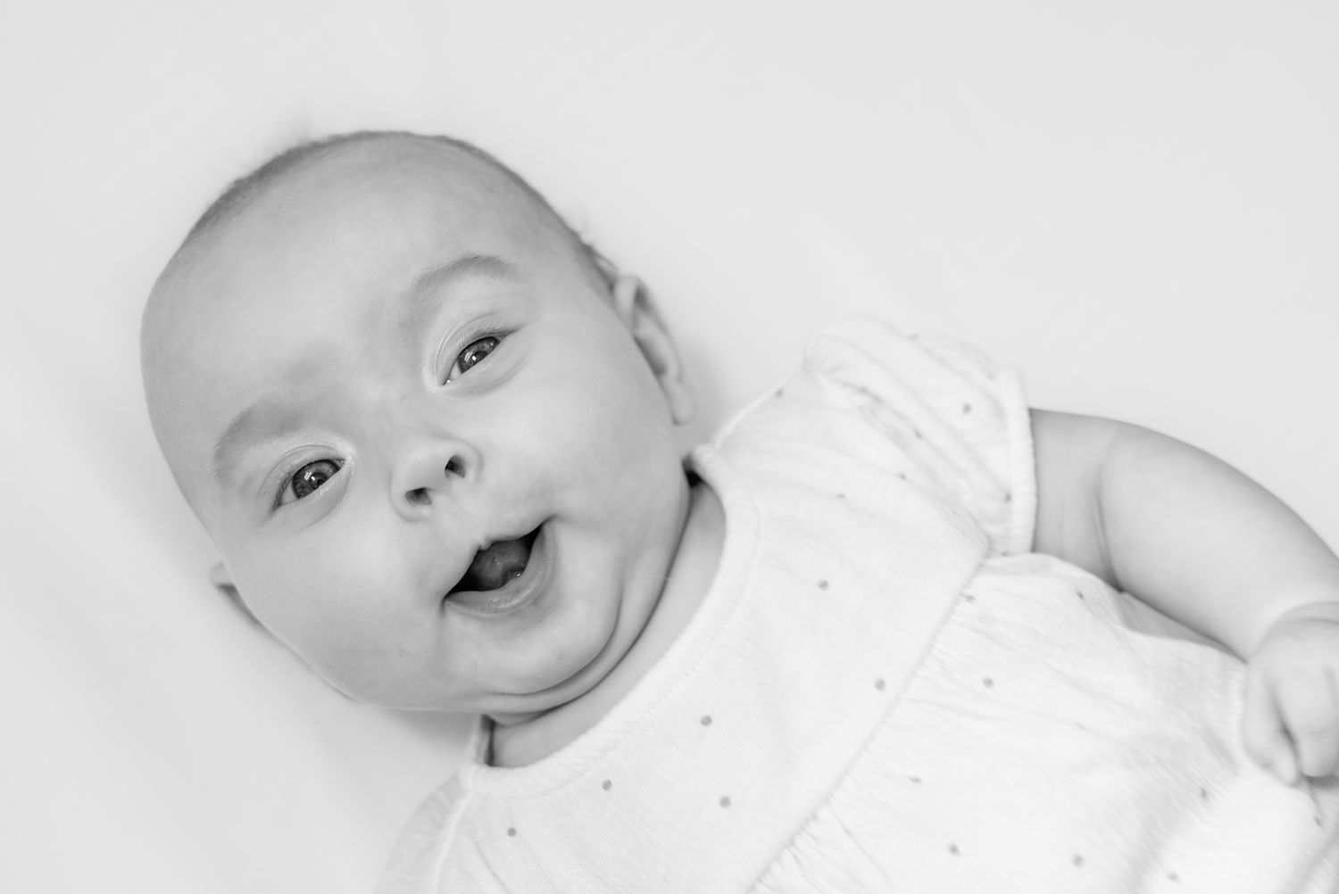 A baby wearing a peach-colored t-shirt lays against a white background looking upward with bright eyes. Quad Cities Newborn Photography