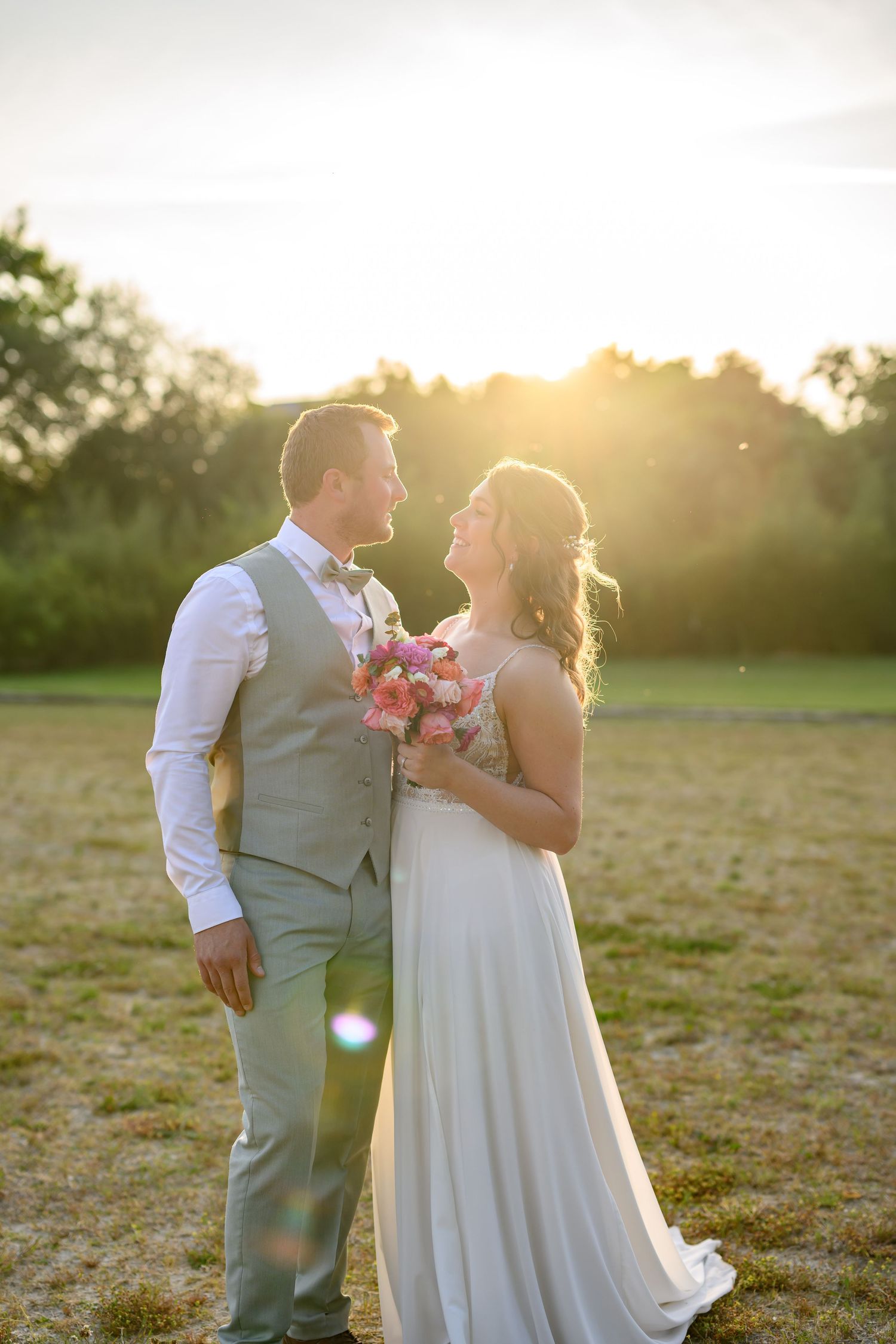 Wedding couple shares romantic moment in golden sunset light in an open field.
