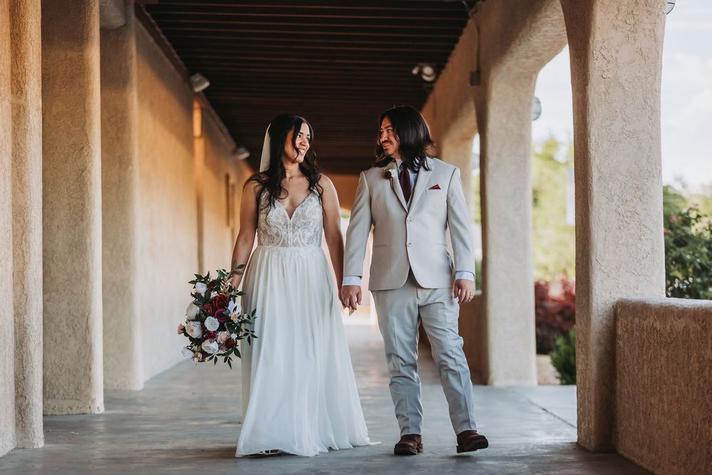 A happy couple embraces in an outdoor venue with white columns and elegant Mediterranean-style architecture.