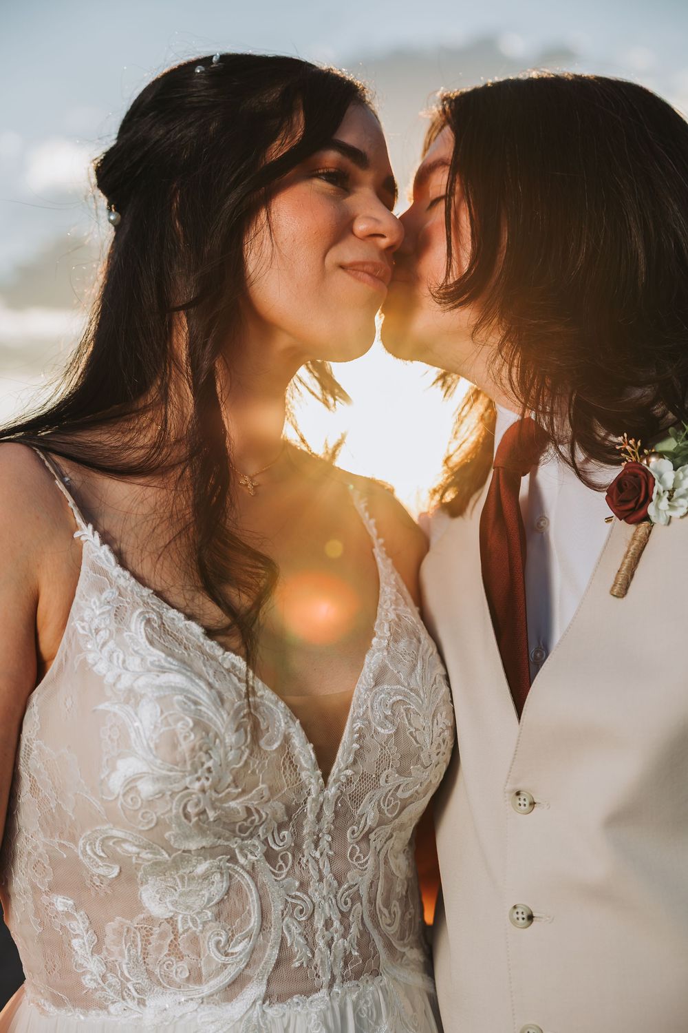 A romantic sunset kiss between a couple in wedding attire with delicate sunlight flare creating a dreamy atmosphere.