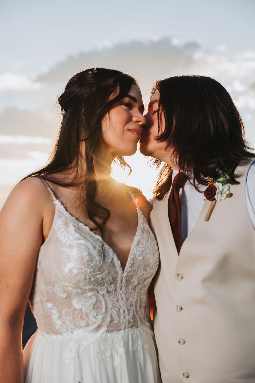 Close up photo of a same sex wedding couple kissing outdoors during sunset in matching white lace gowns.