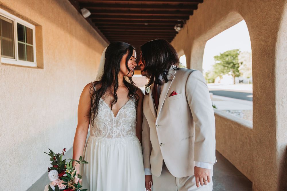 Wedding couple stands in a covered walkway with exposed wood beams and Adobe-style architecture.