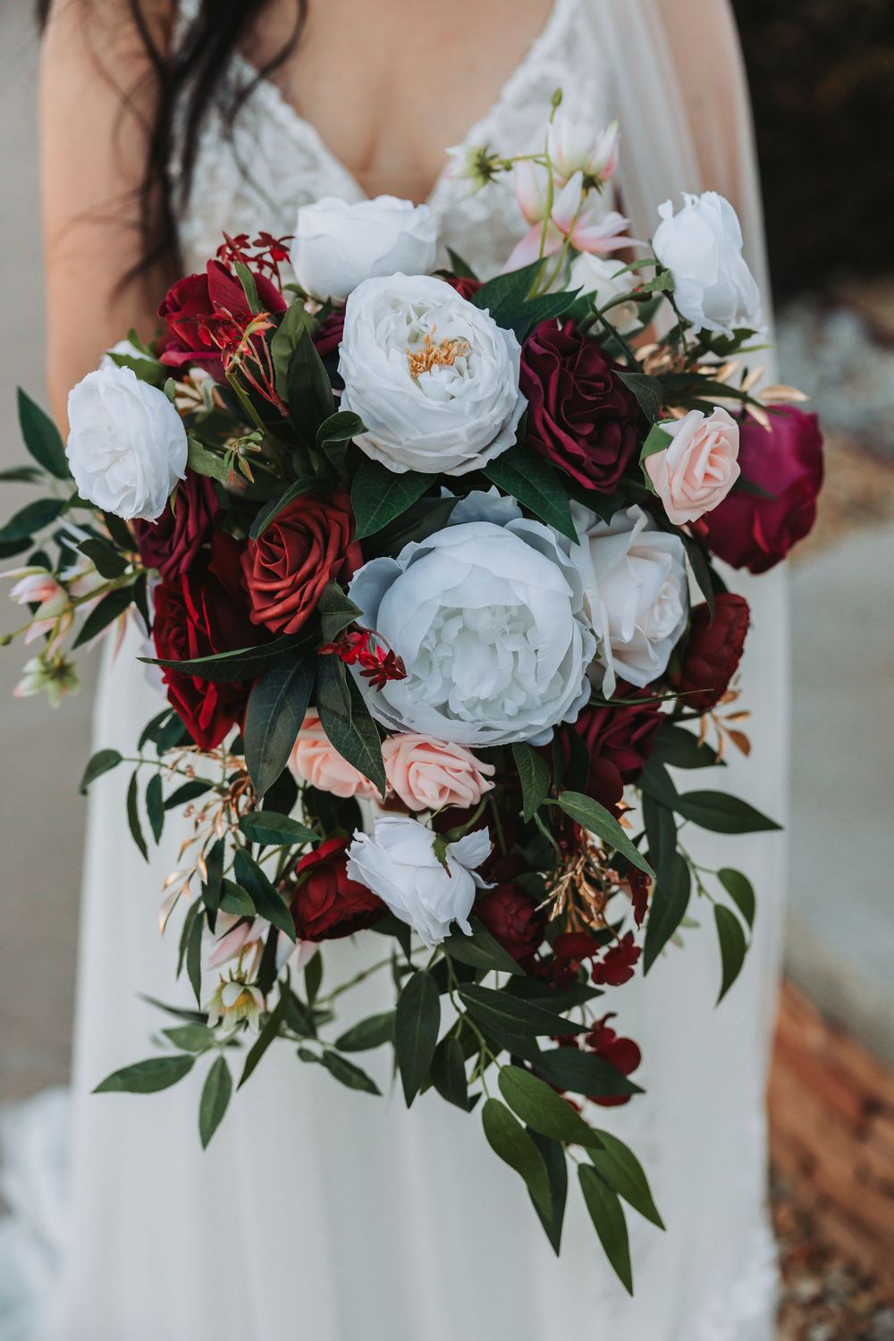 A stunning wedding bouquet featuring burgundy roses, white peonies, and lush greenery creates elegant contrast.