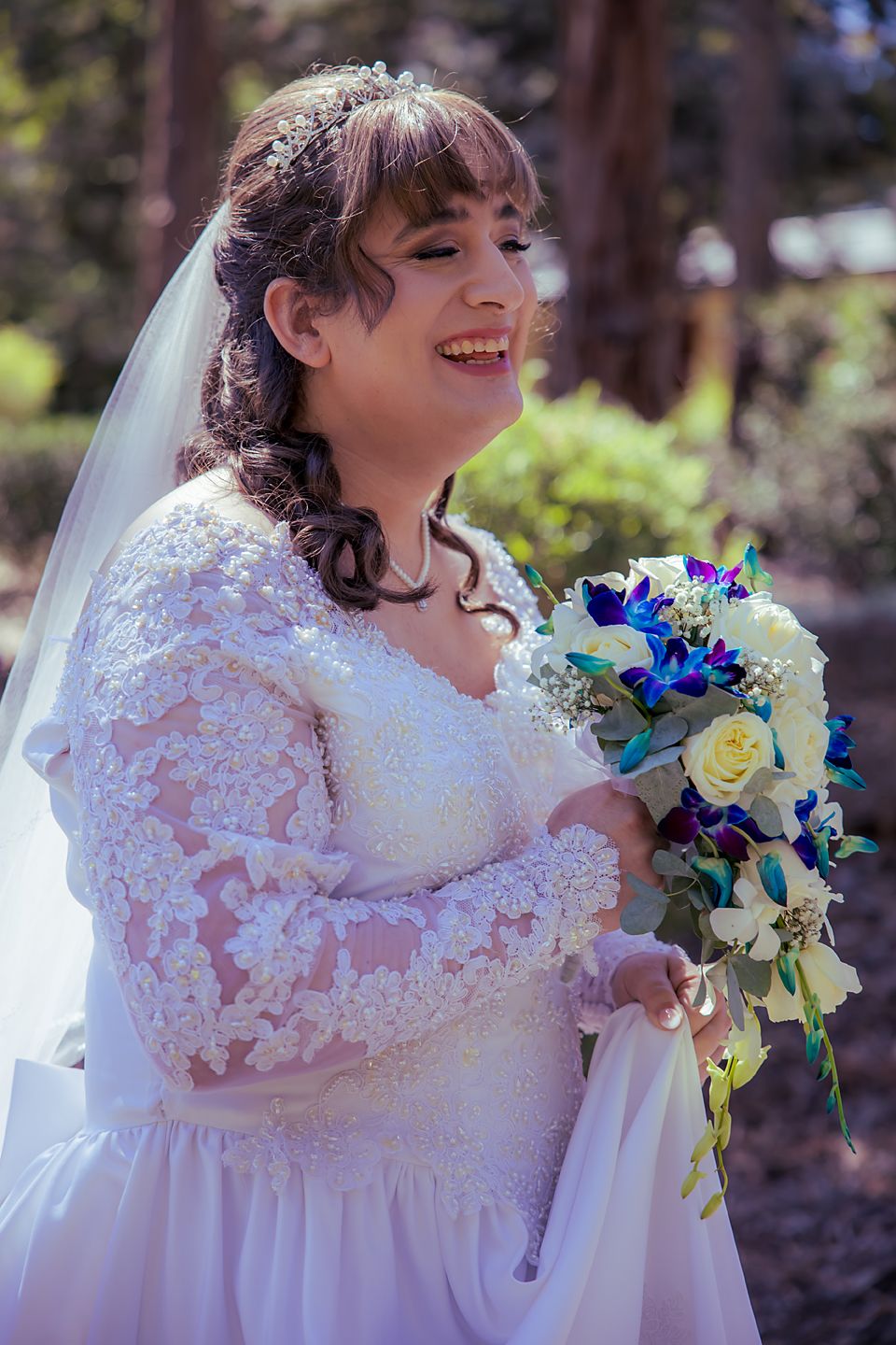 Beautiful wedding dress with lace sleeves and a bouquet featuring blue and white flowers in an outdoor setting.