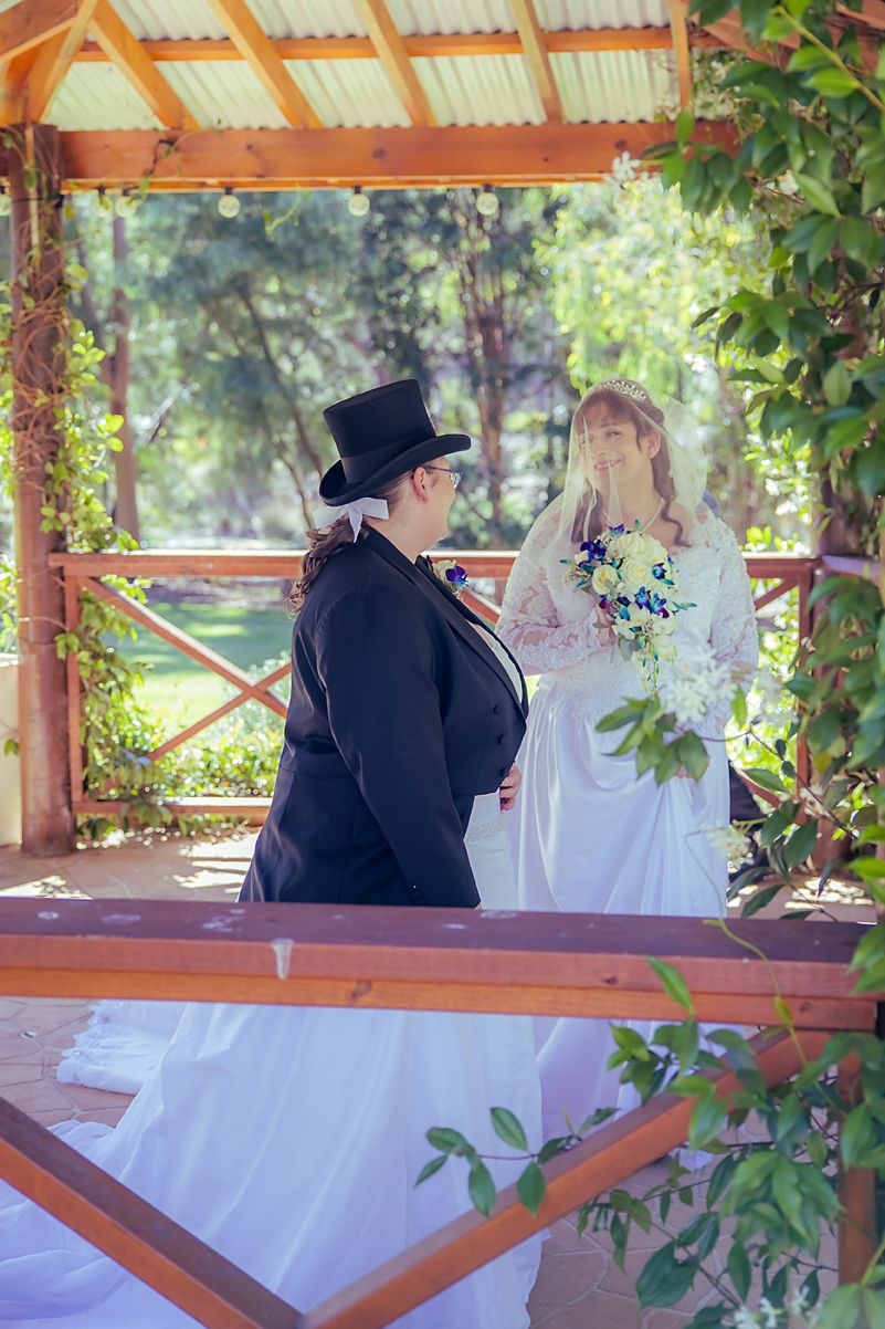 Couple shares an intimate moment in a rustic wooden gazebo with greenery and natural light.