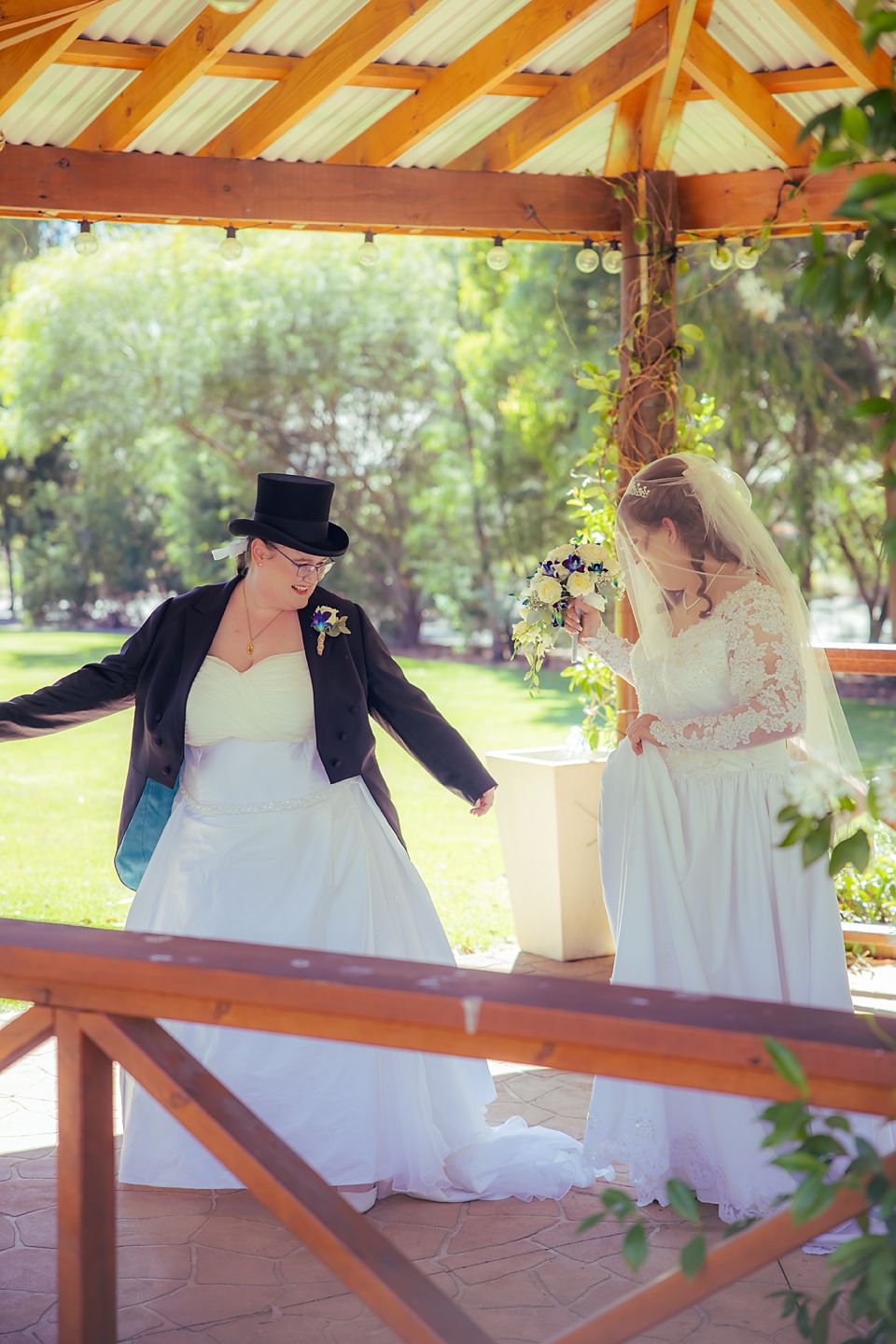 Romantic couple in wedding attire share an intimate moment under a rustic wooden gazebo.