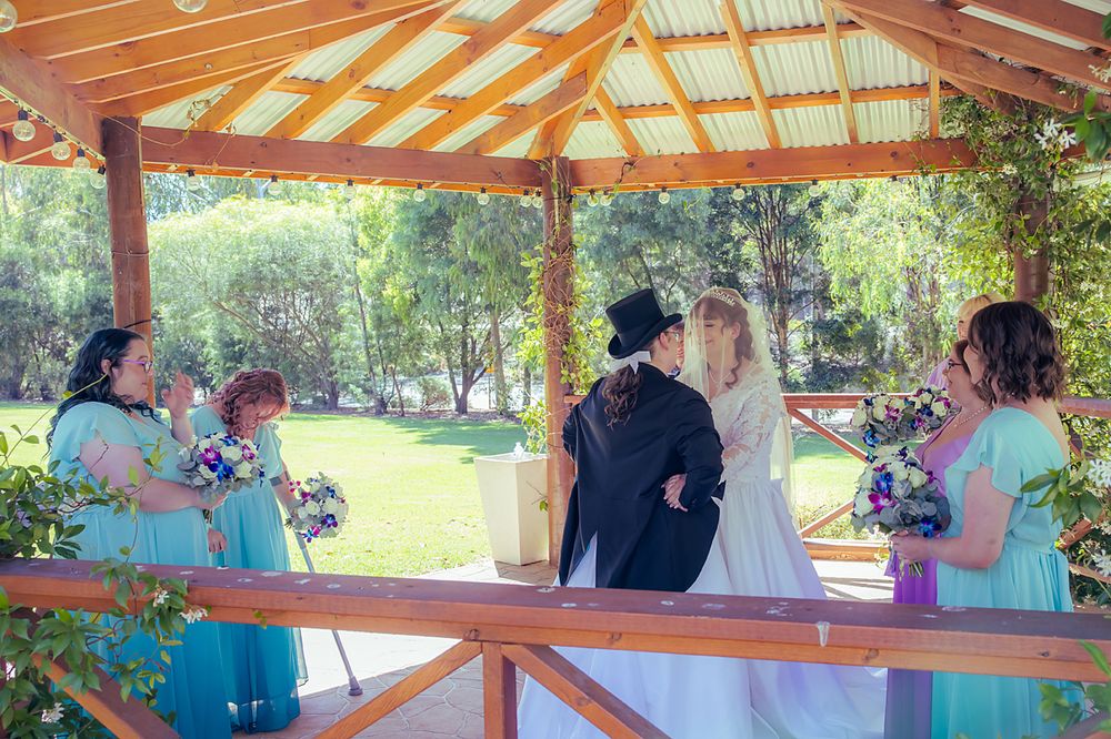 A celebratory gathering takes place under a rustic wooden pavilion with blue and white decorative elements.