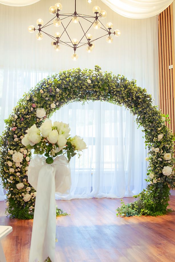 A wedding ceremony venue with elegant floral arches and white draping creating a romantic indoor backdrop.