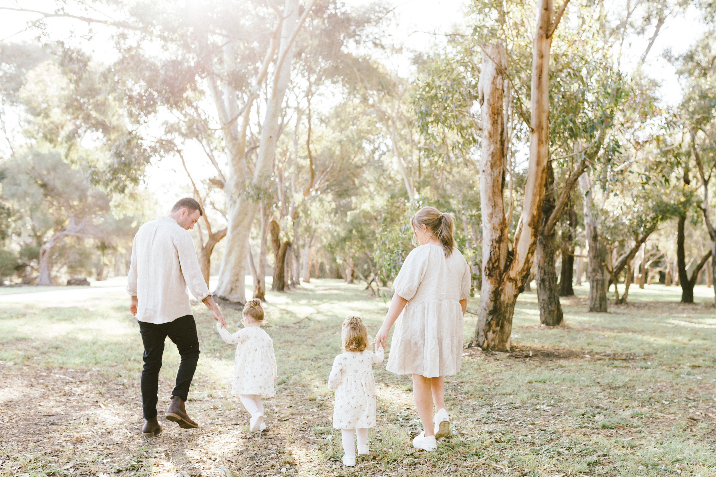 A romantic couple strolls together through a sun-dappled eucalyptus grove in white attire during an outdoor photo session.