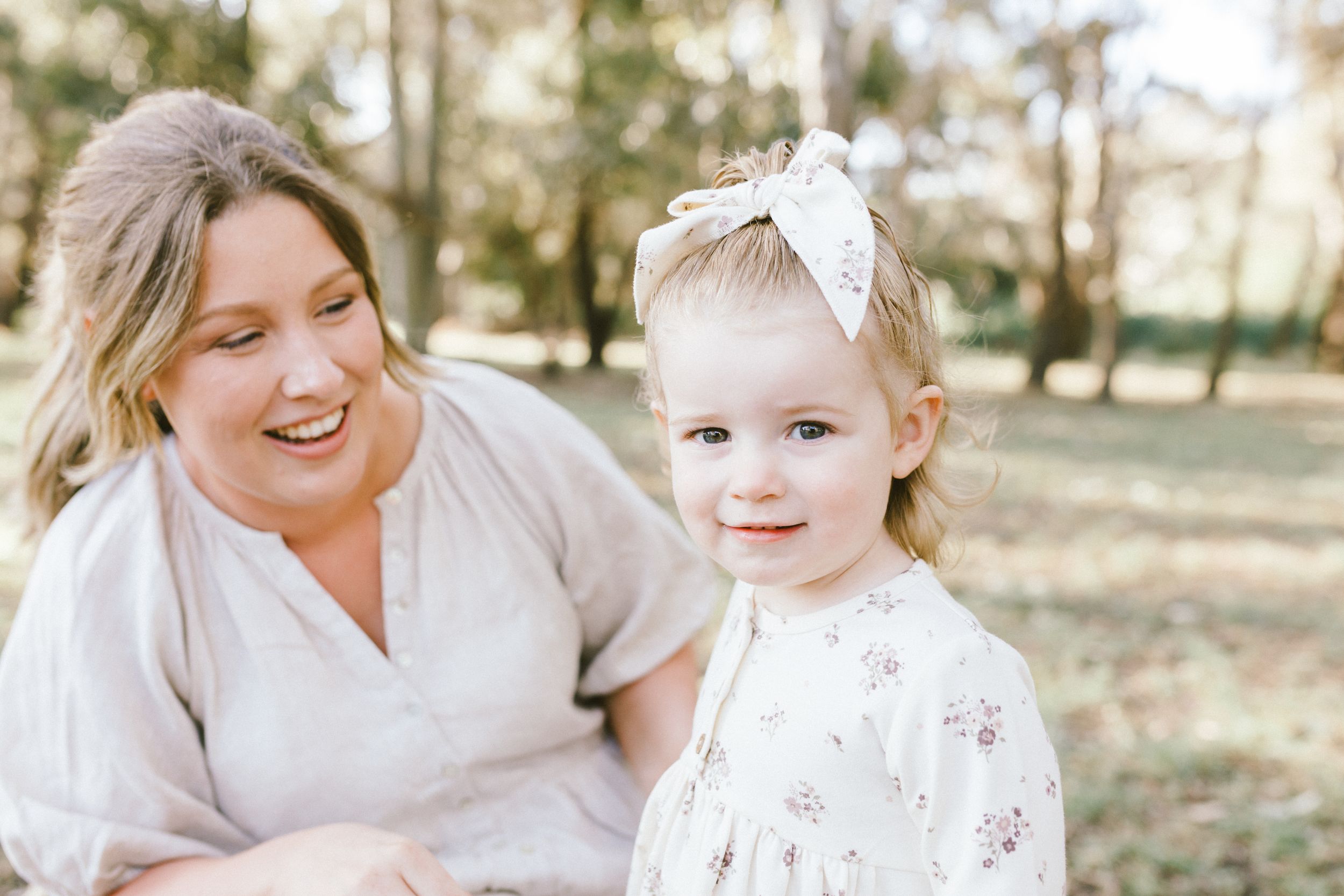 A sunny outdoor portrait shows a touching moment between parent and child sitting together in a natural setting.