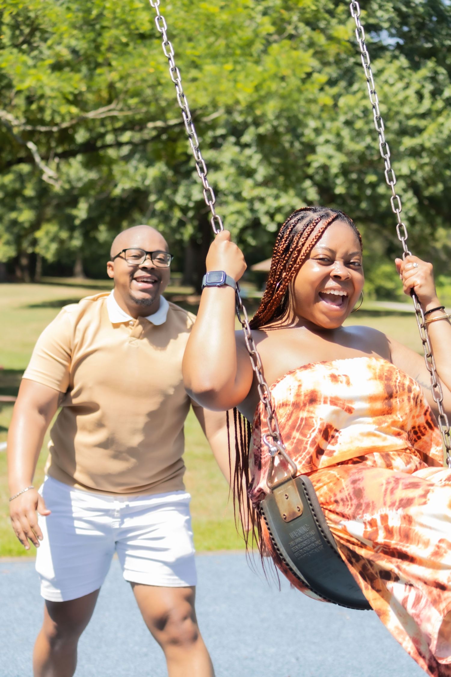 A person in an orange and white dress enjoys swinging at a park on a sunny summer day, showing expressions of pure joy.