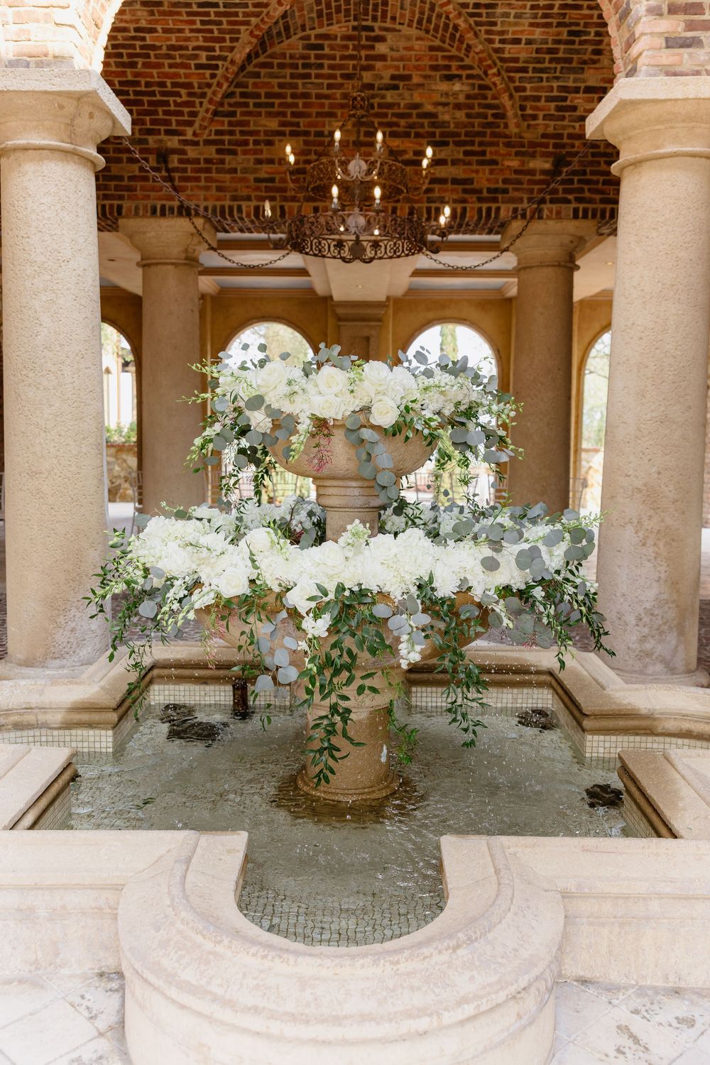 Beautiful white floral arrangements decorate elegant stone columns in an arched brick courtyard.