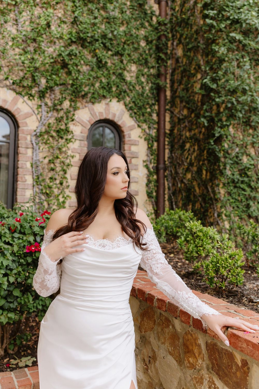 Elegant white wedding dress with lace sleeves photographed against a stone wall covered in green vines.