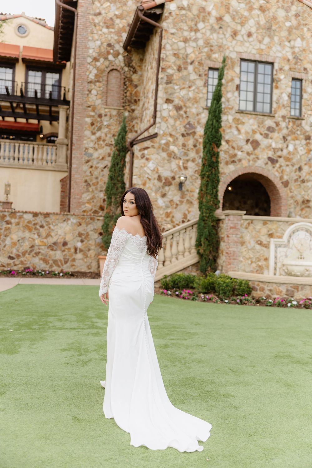 Elegant white wedding gown photographed against stone architecture and manicured lawn.