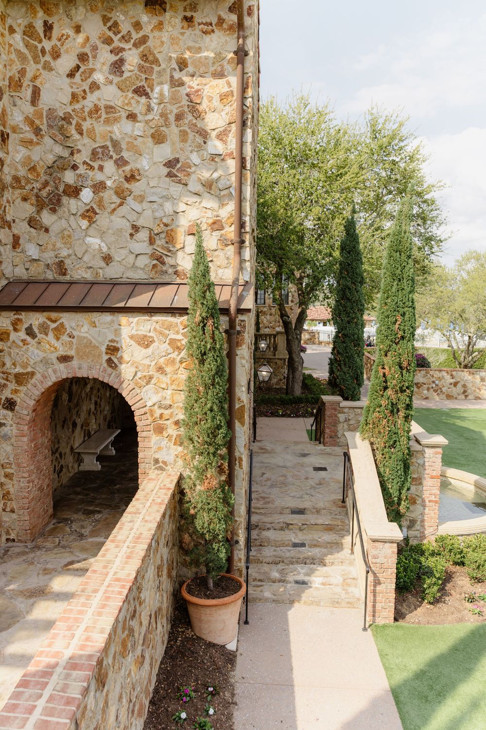 Stone archway walkway with brick flooring and climbing vines along a rustic Mediterranean-style building.