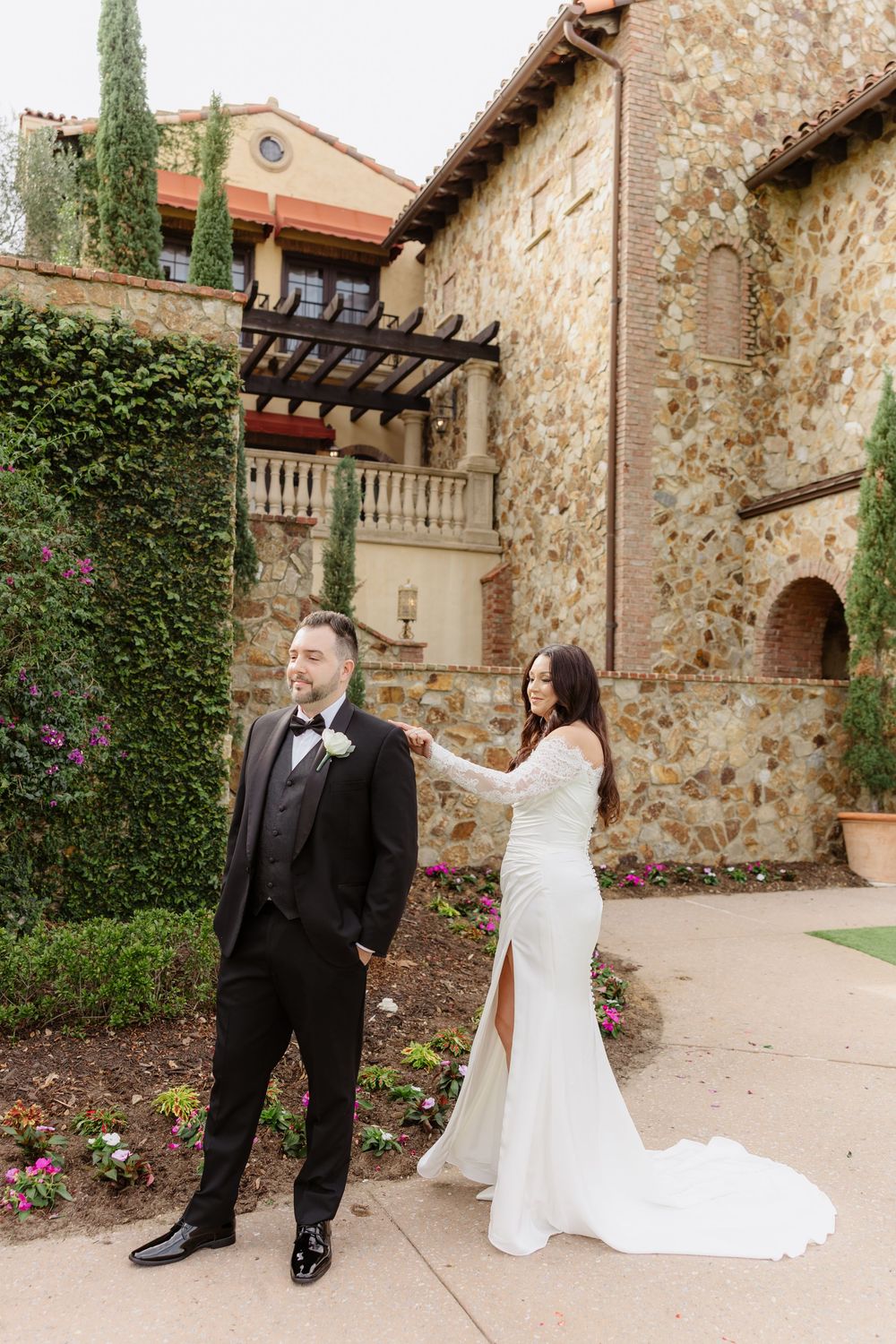 An elegant wedding celebration takes place in front of a rustic stone wall with ivy and climbing roses.