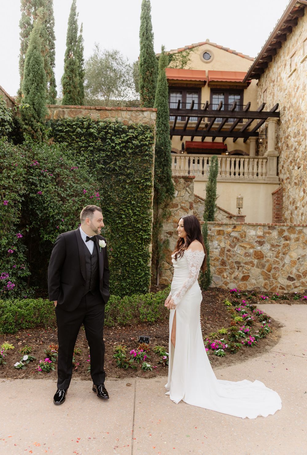 A couple shares romantic moments in a Mediterranean-style courtyard with stone walls and cypress trees.