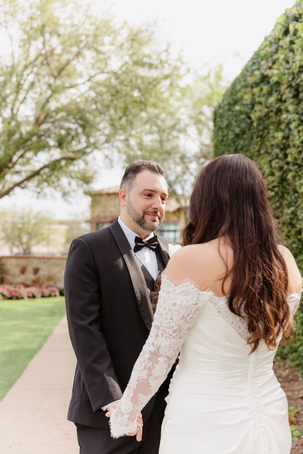 Romantic first look moment between newlyweds outdoors in springtime setting with blossoming trees.