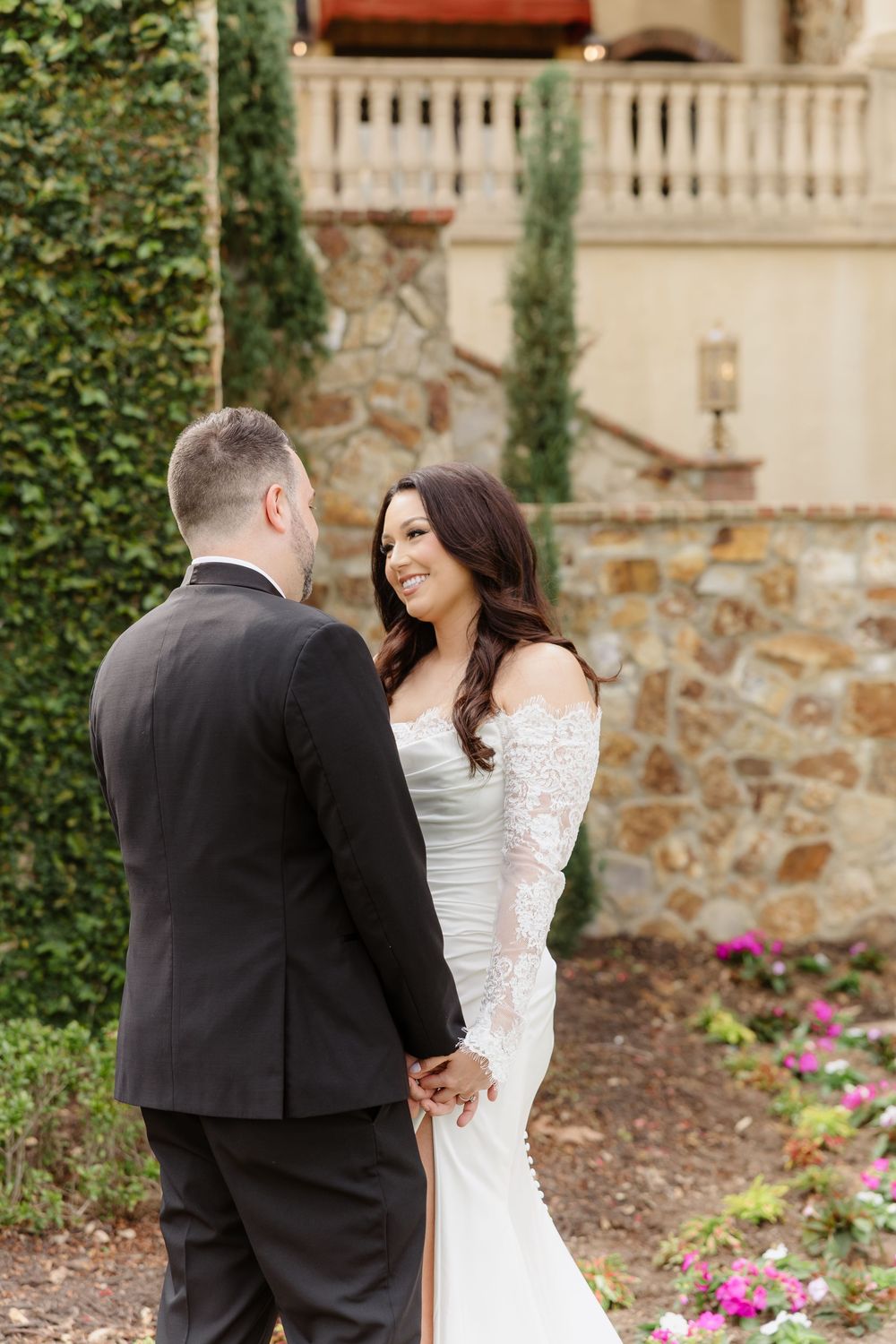 Wedding couple shares intimate moment in garden courtyard with stone walls and ivy backdrop.