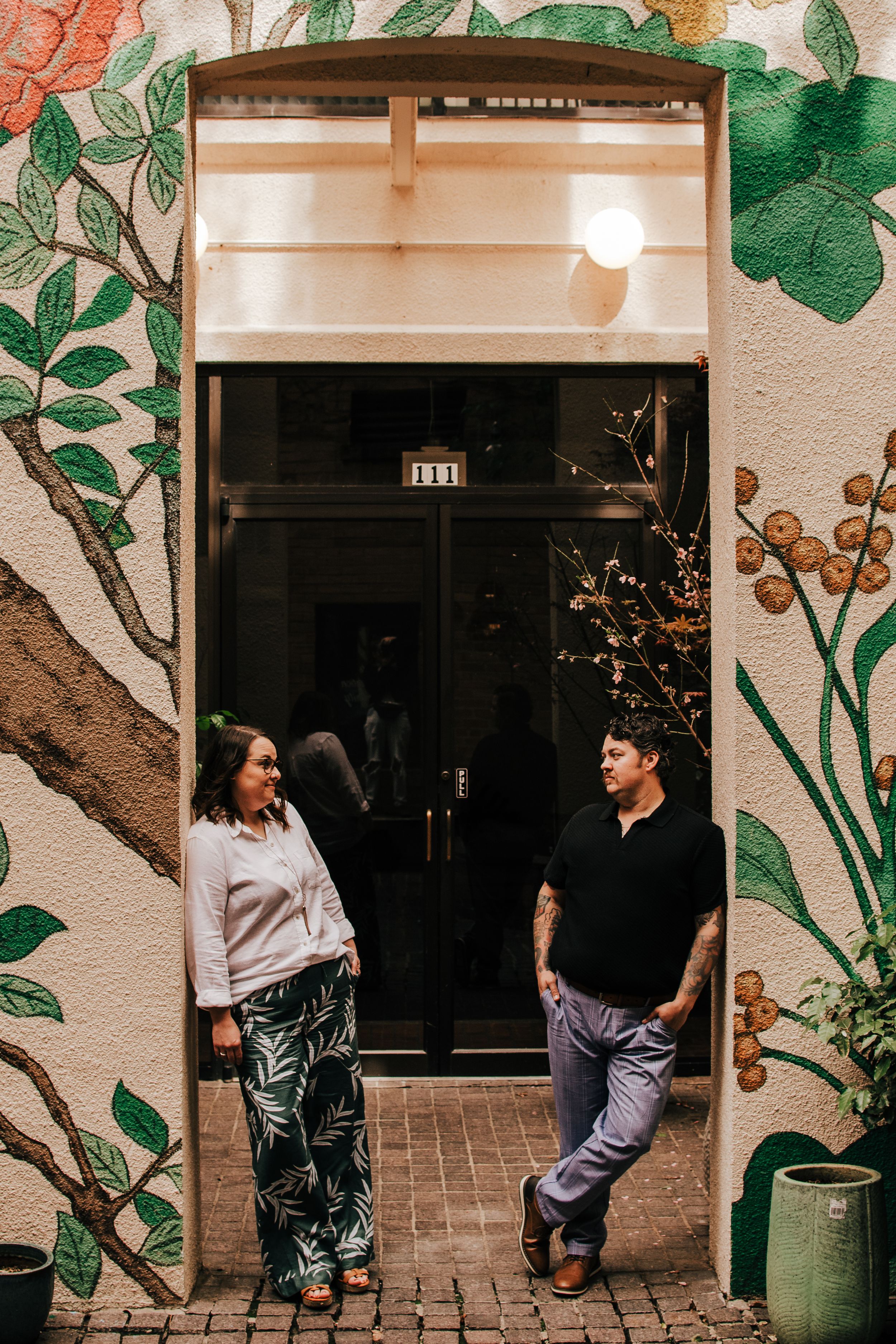 A series of five connected photos showing two people sitting and interacting along a wall with green floral artwork.