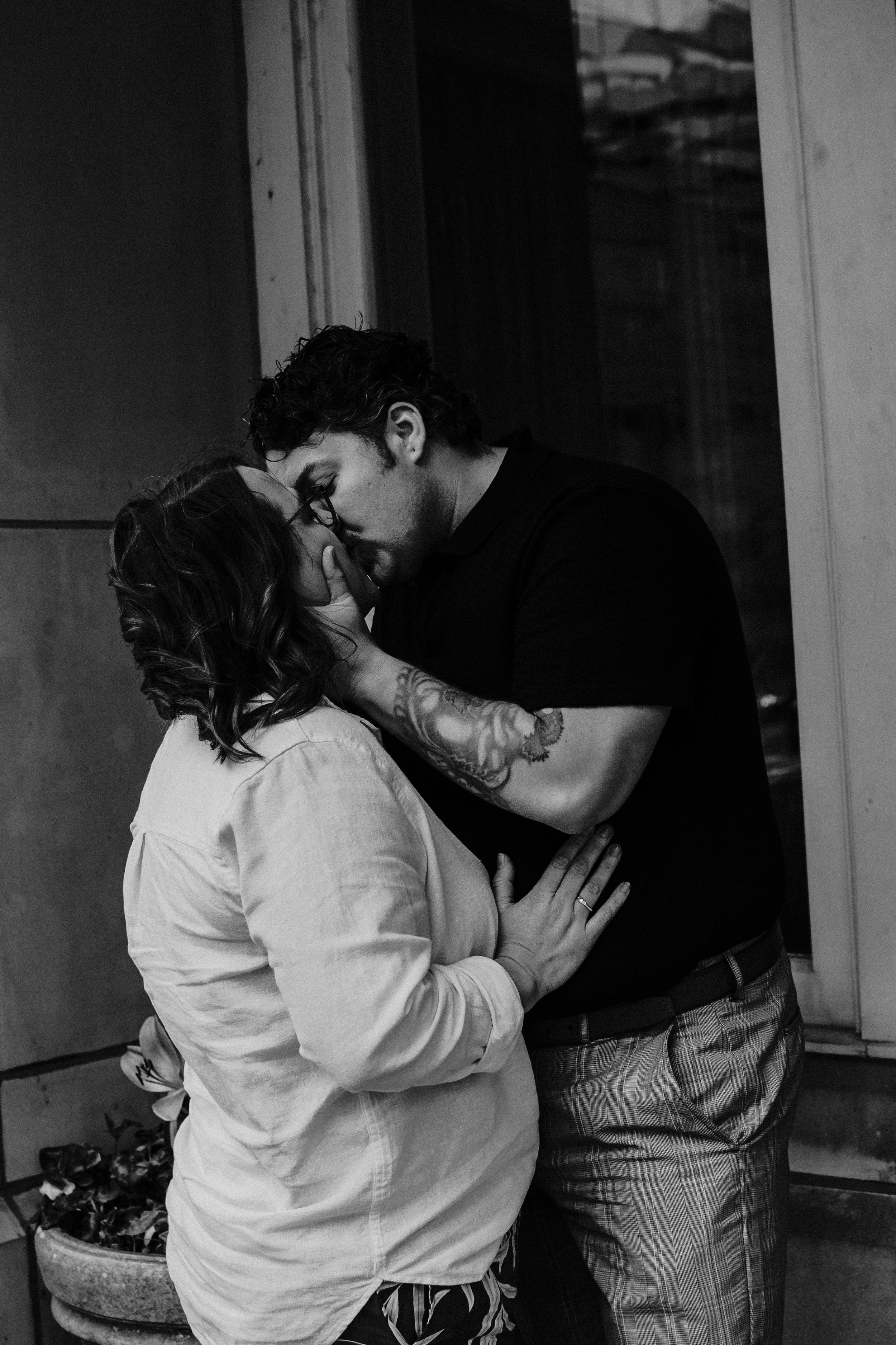 Two figures embrace in an intimate black and white moment near a doorway.