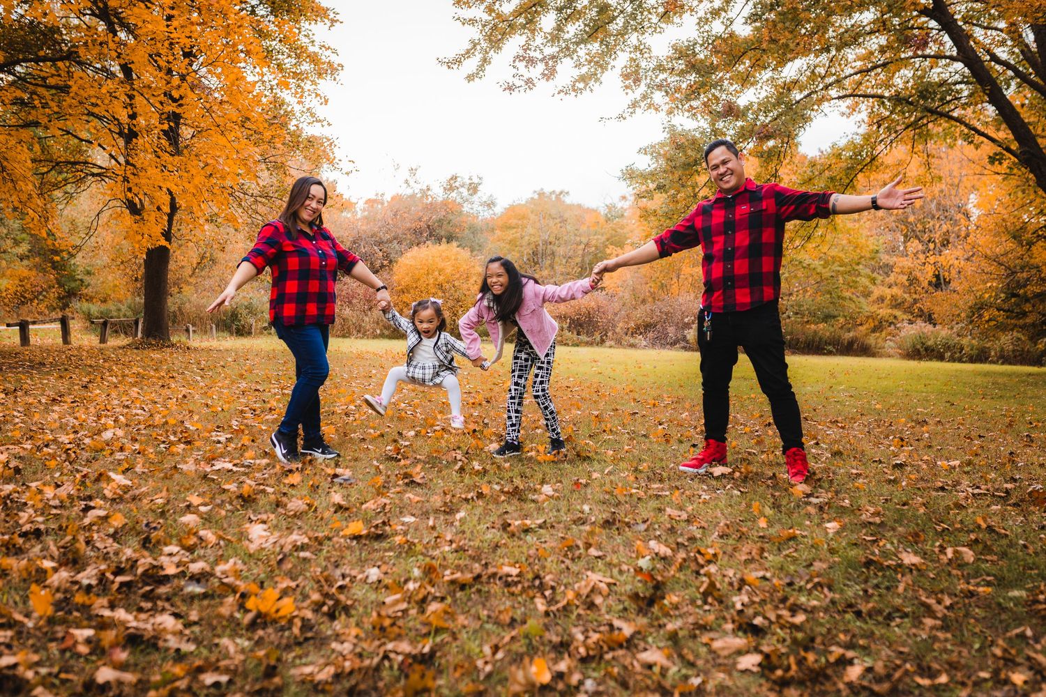 A family enjoys a playful autumn day in the park surrounded by golden fall foliage and scattered leaves.