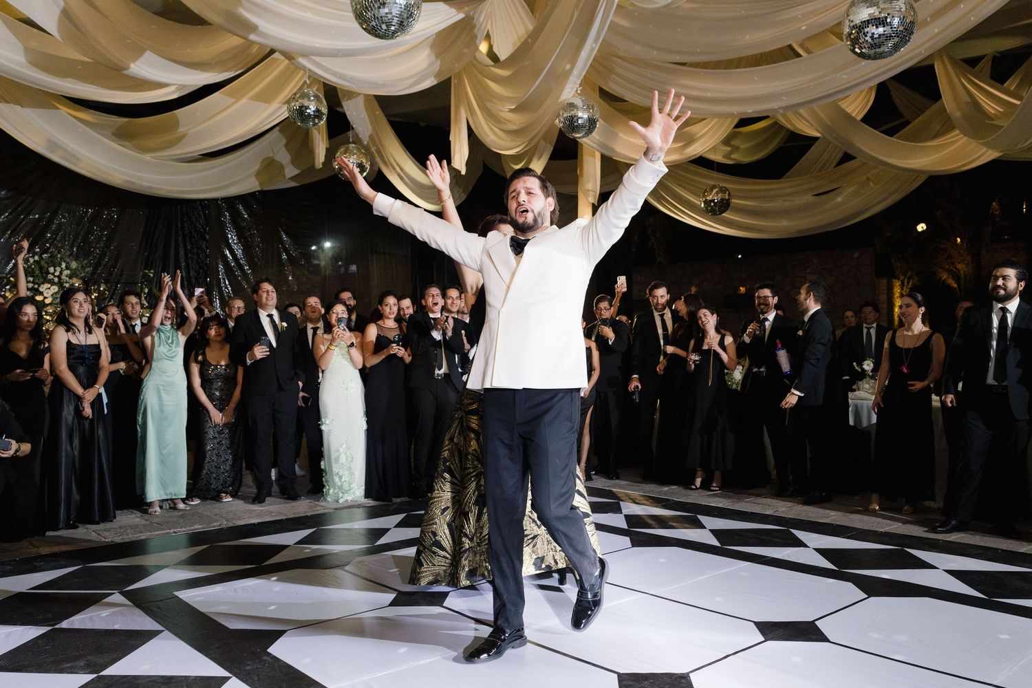 Wedding reception dance floor with guests celebrating under draped white fabric ceiling.
