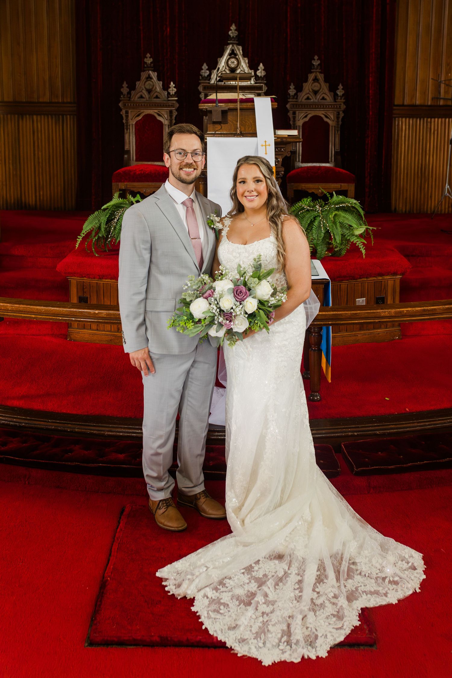 Elegant wedding couple poses in church sanctuary with dramatic red carpet and ornate Gothic architecture backdrop.