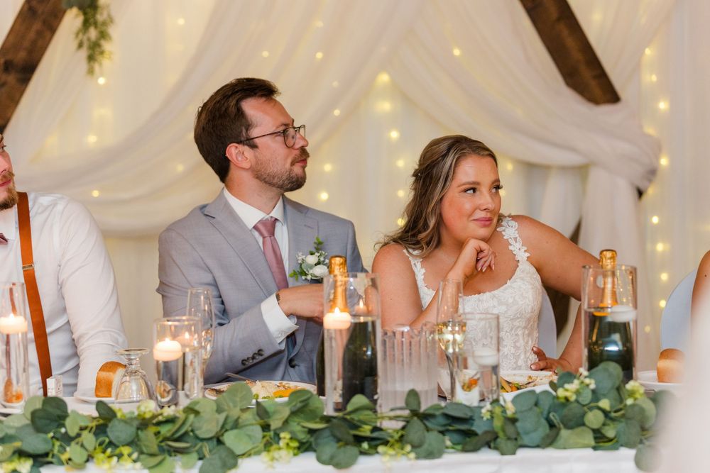 A couple laughs during their wedding reception at a head table decorated with greenery and candlelight.