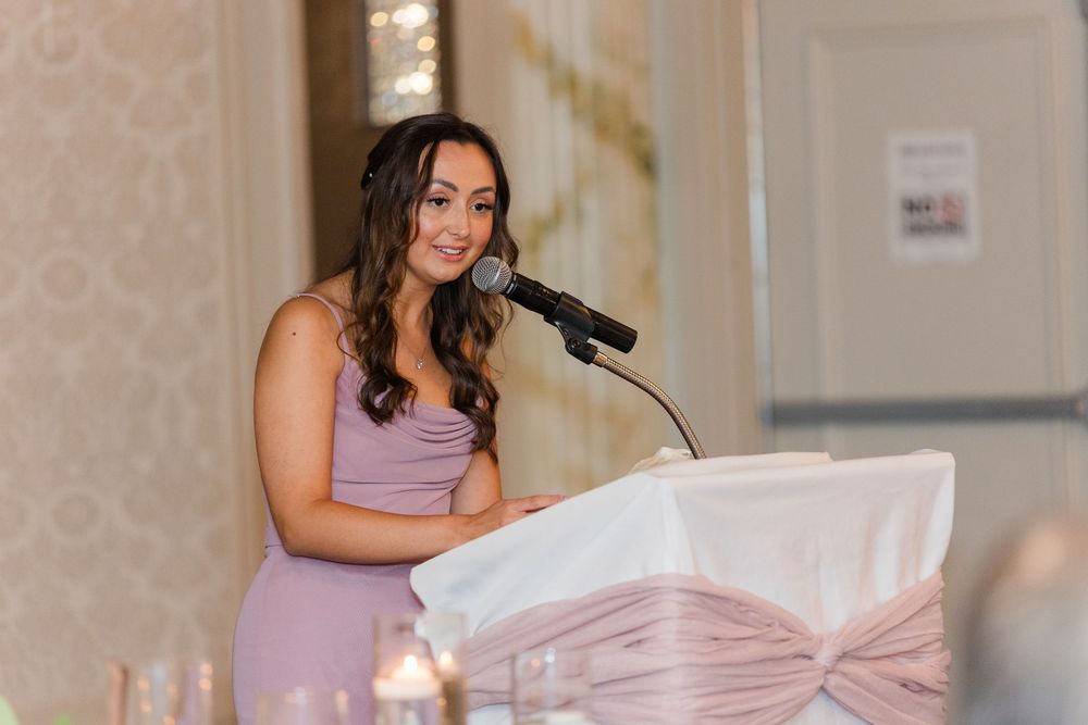 Wedding party members in light purple dresses hold microphones and deliver heartfelt speeches during the reception.