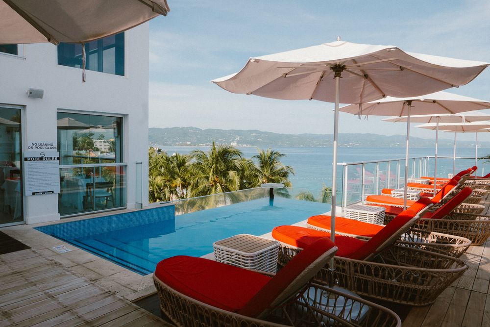 Modern hotel rooftop terrace featuring orange lounge chairs and umbrellas with stunning ocean views.