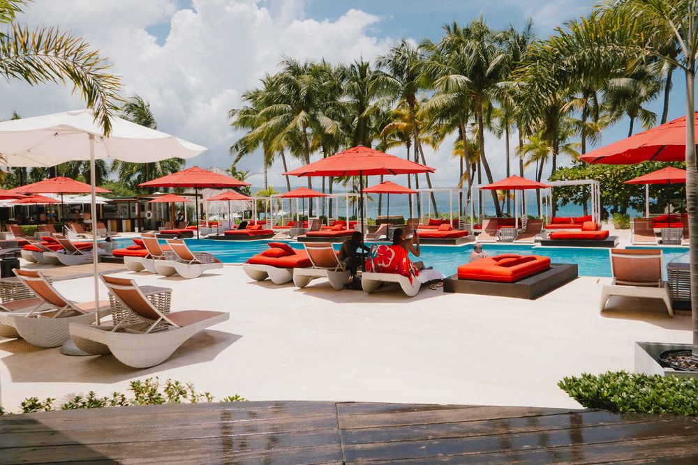Luxury beachside resort lounge area with red cushioned daybeds and palm trees overlooking a pristine ocean view.