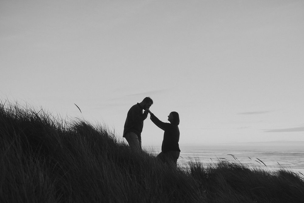 Silhouettes of a couple against a dramatic sunset sky with tall grass in the foreground.
