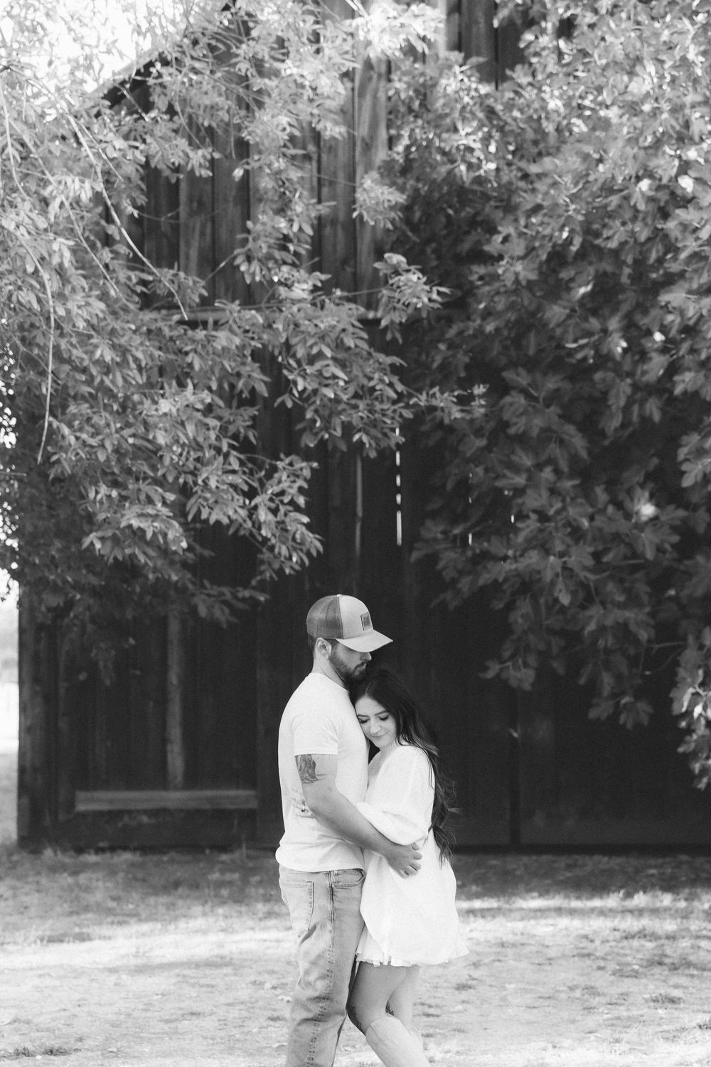 A romantic black and white photo series of a couple embracing under leafy trees.