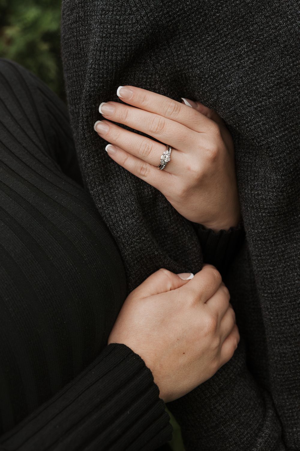 Close-up view of hands wearing a black knit sweater with a sparkling diamond engagement ring on display.