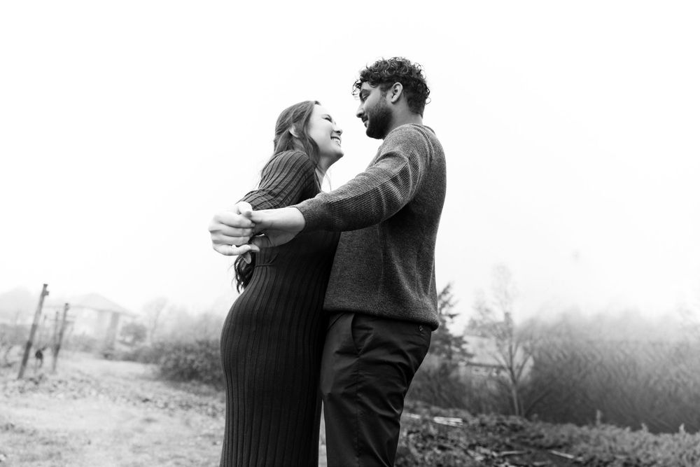 A romantic black and white photograph of a couple embracing outdoors on a misty day.
