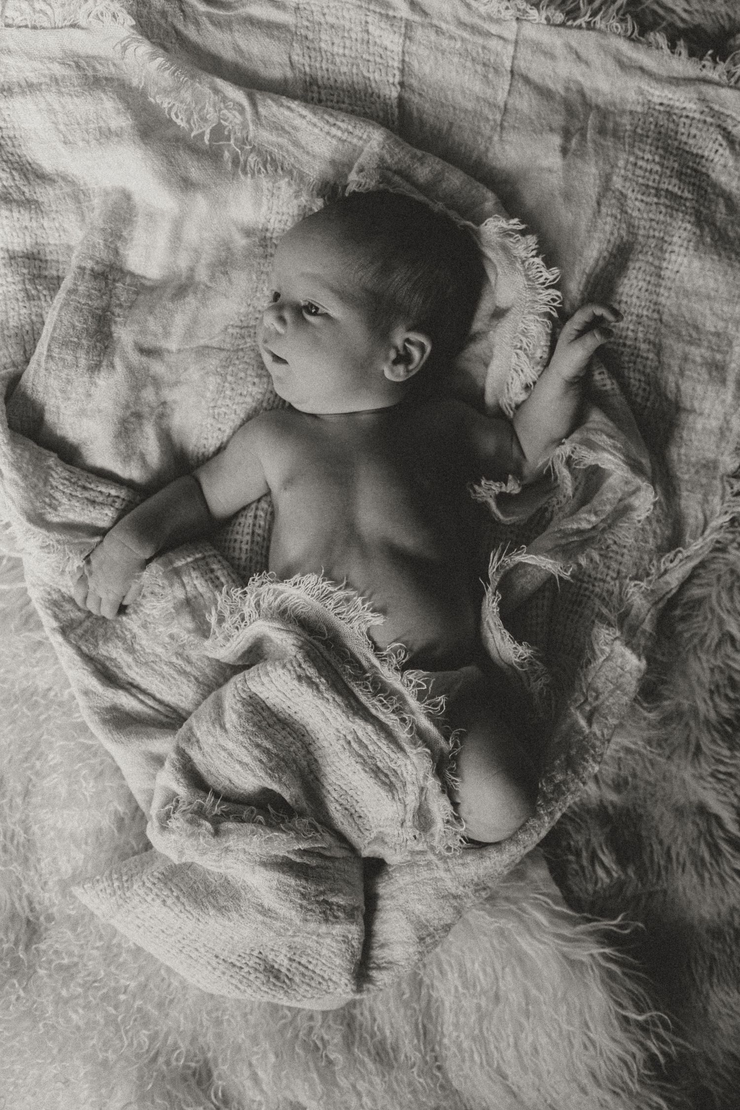 Black and white artistic photographs of baby resting on textured blankets with dramatic shadows.