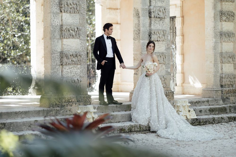 Romantic wedding couple poses against stone pillars in an elegant outdoor setting with soft lighting.