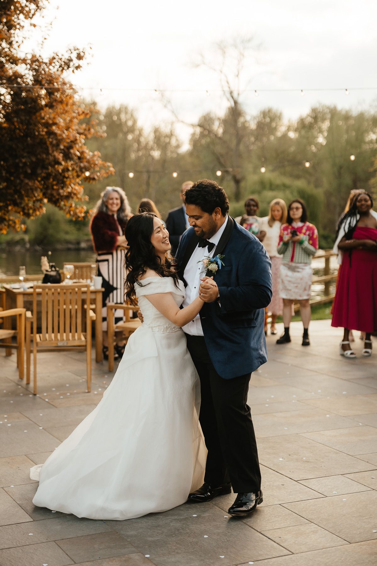 A newlywed couple share their first dance together at an outdoor wedding reception during golden hour sunset.