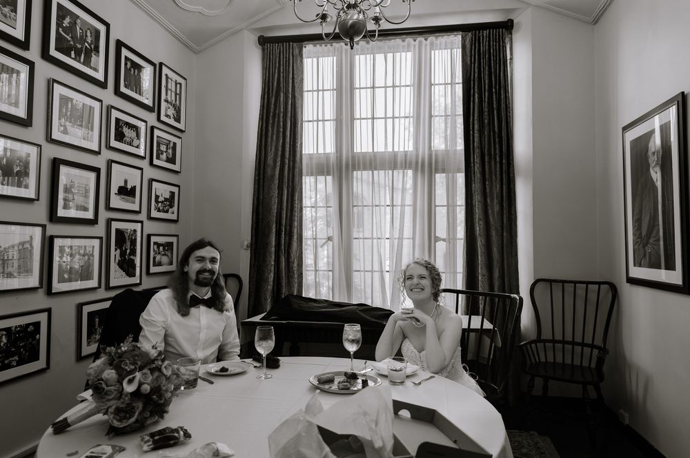 Black and white panoramic photograph showing a person sitting in an elegant dining room surrounded by framed artwork.